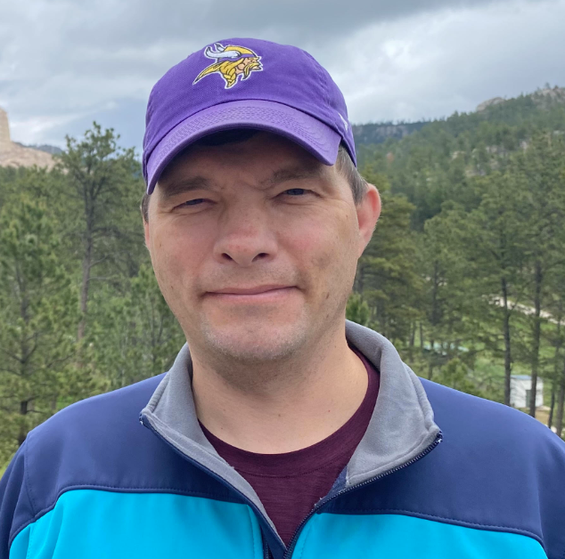 Headshot of Chris Hofer wearing a purple Minnesota Vikings cap and a blue jacket in an outdoor setting